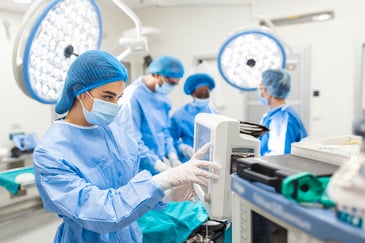 a surgeon works on a screen in an operating room as additional doctors convene in the background